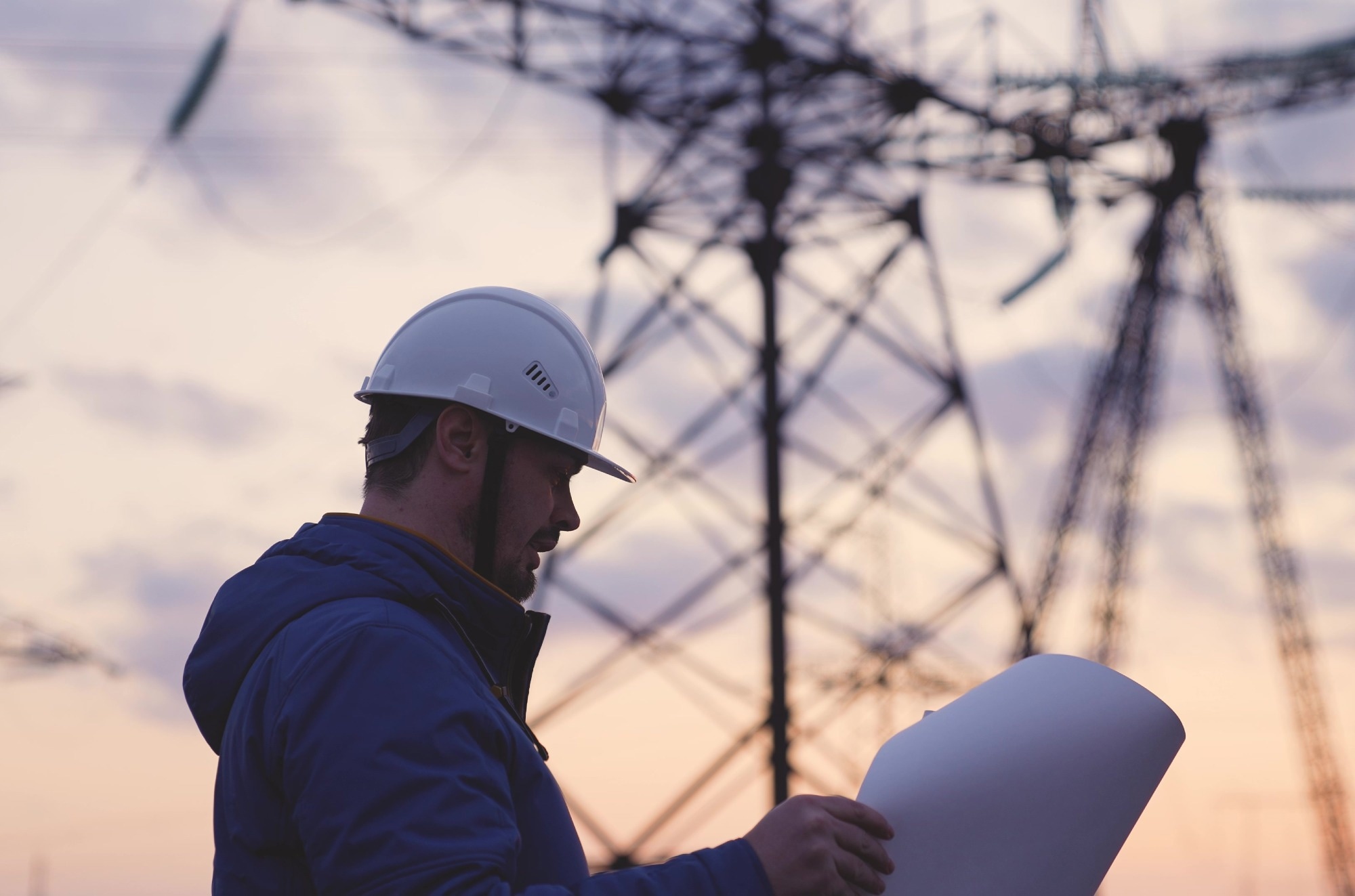 An electrician on the background of high towers of power plants looks at the project for the development of an electrical structure, the expansion of the electrical voltage of volts in the wires