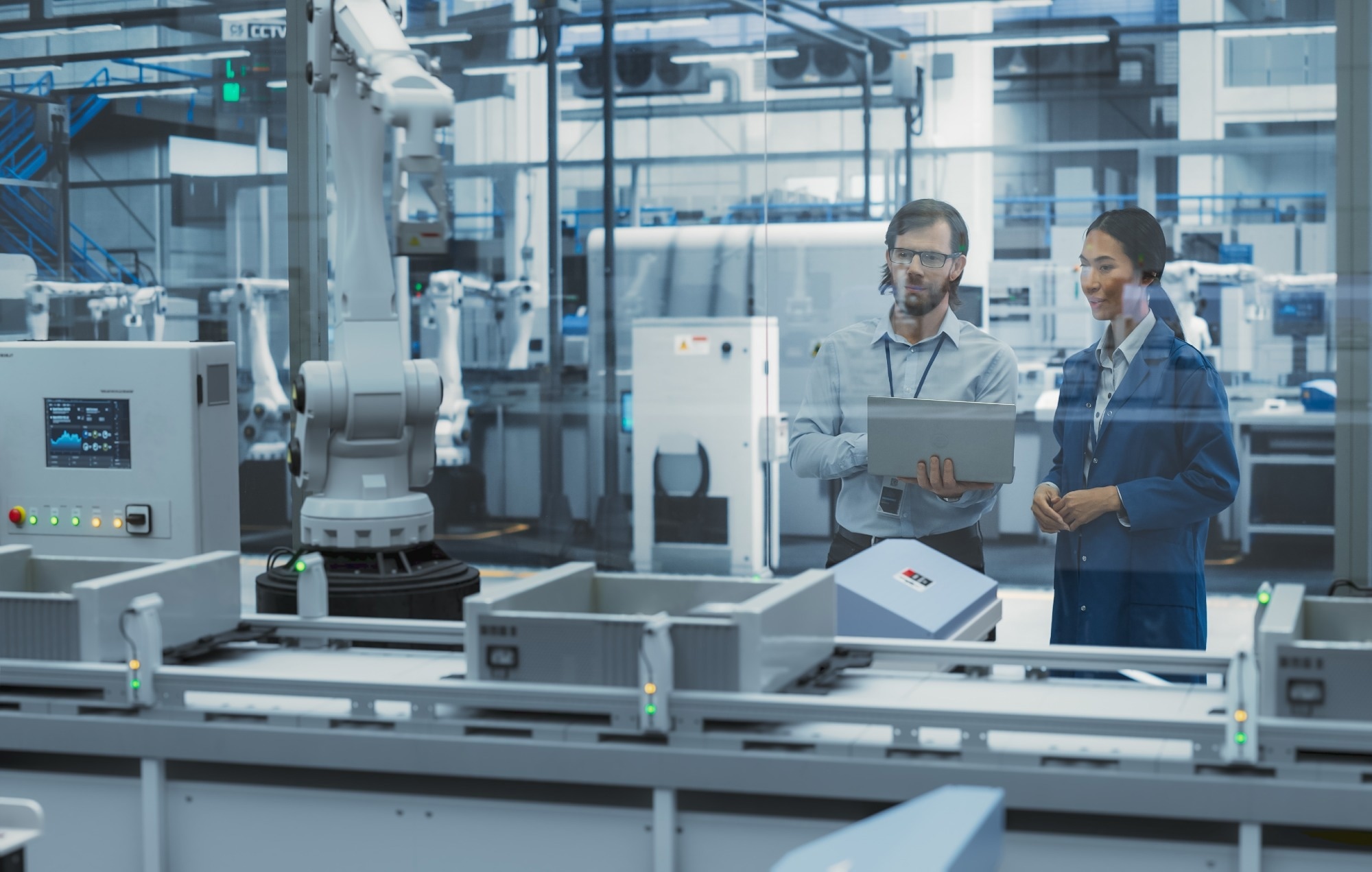 Engineers monitor assembly robots on a production line, using laptops to oversee IIoT systems.