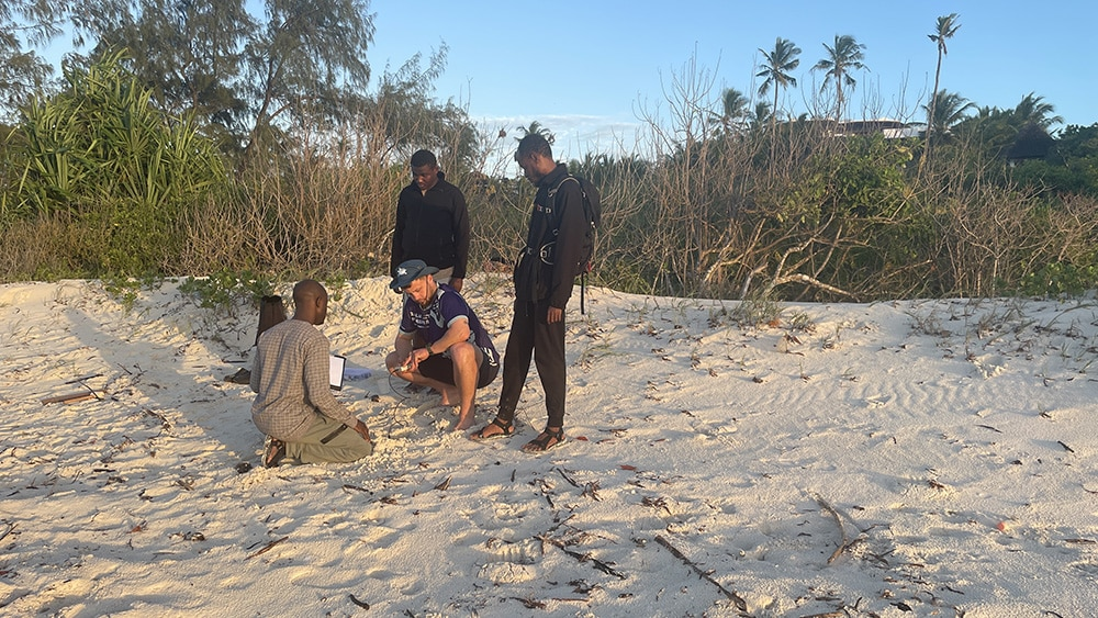 Four members of the collaborative team standing on the beach, analyzing nest data using the WET150 sensor.