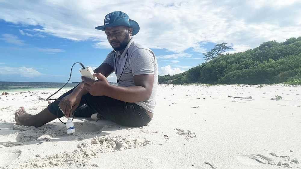 Joe Ngunu Wandiga from LOC sat on the beach, taking a portable reading from a WET150 Sensor.