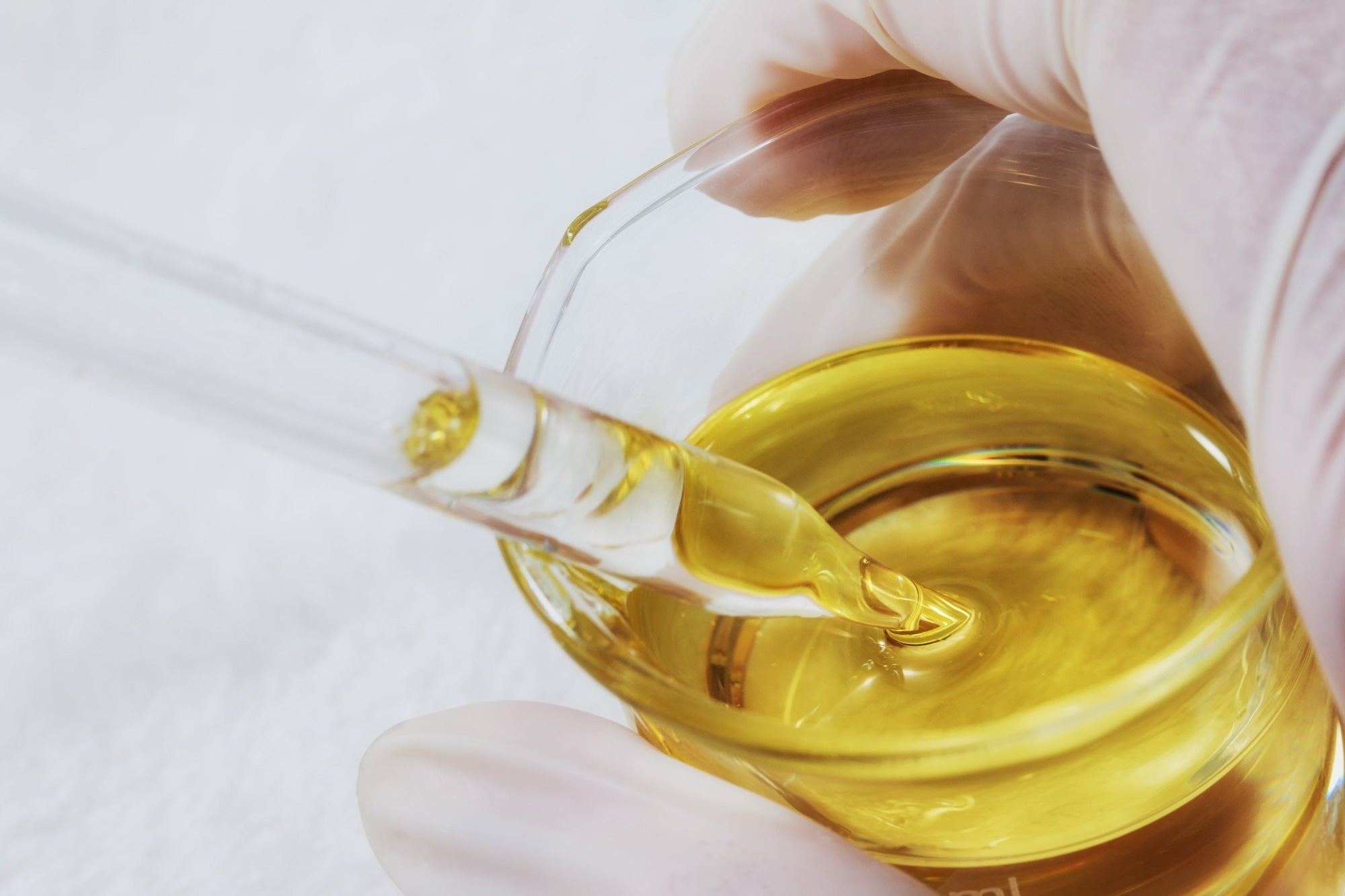 A scientist uses a glass pipette to extract oil/lubricant from a beaker.