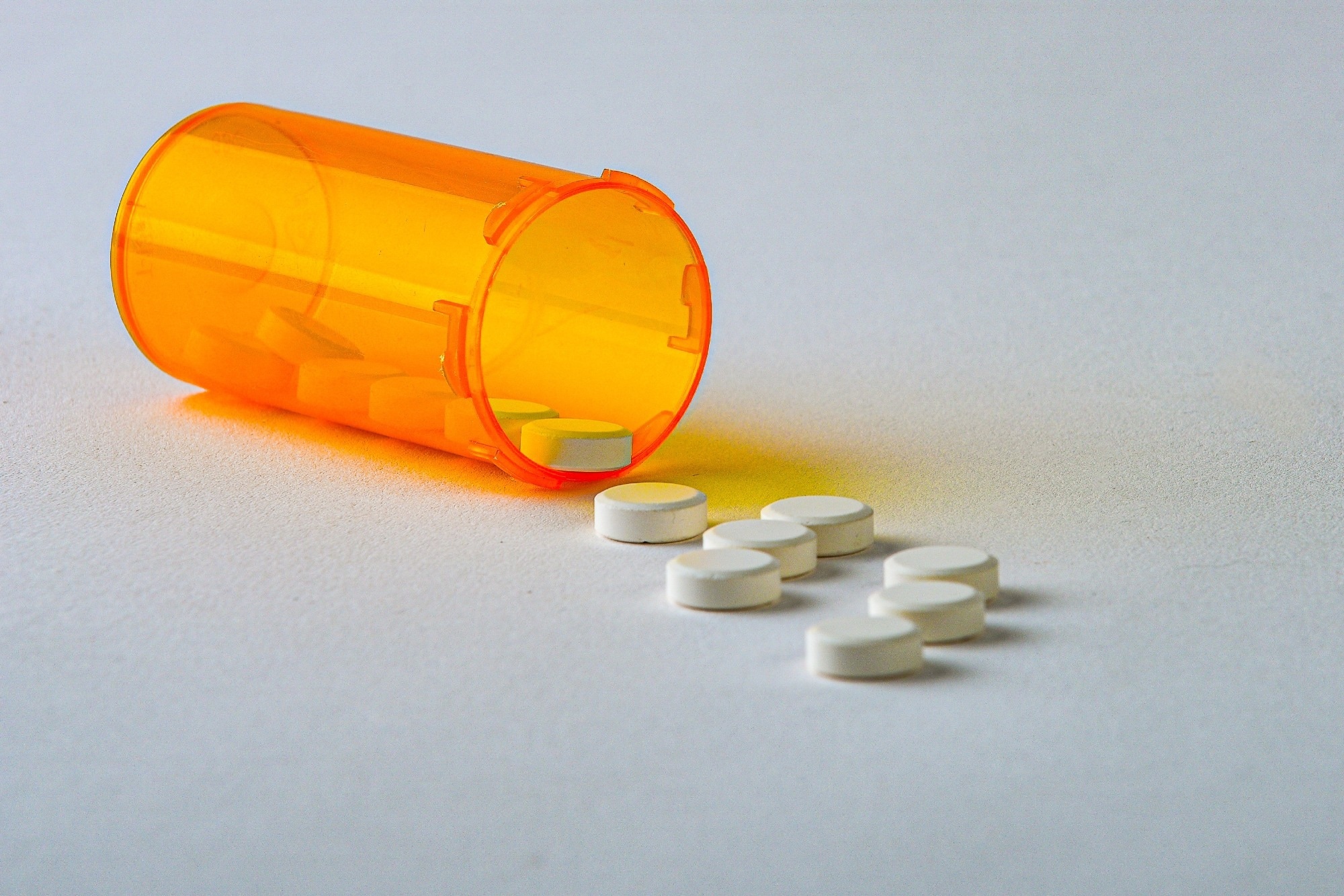 Opioid tablets falling out of an orange table case, onto a white surface.