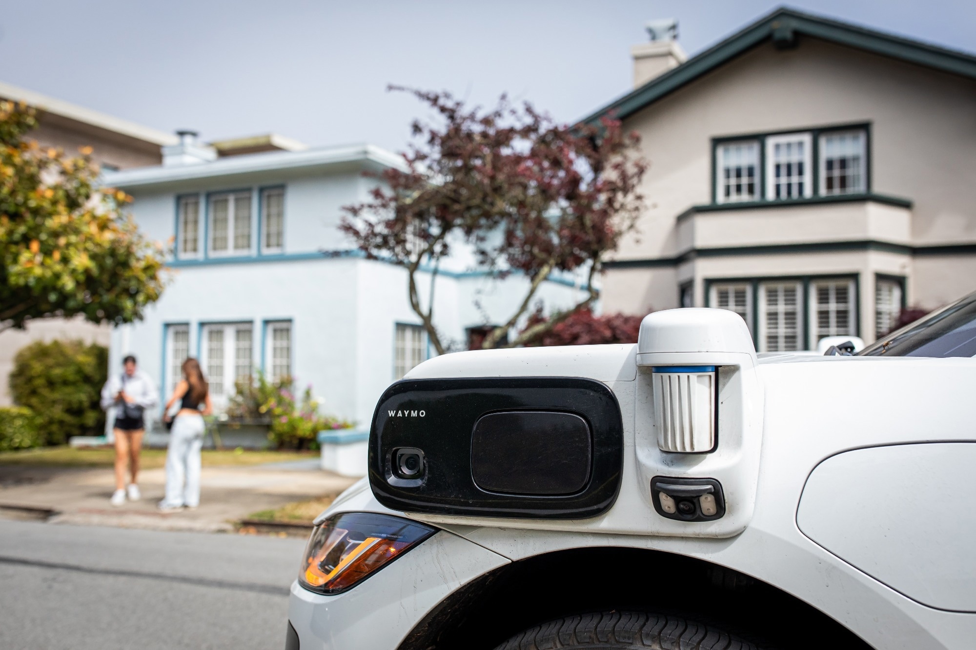 a Waymo autonomous vehicle, recognizable by its distinct sensor array, parked on a residential street.