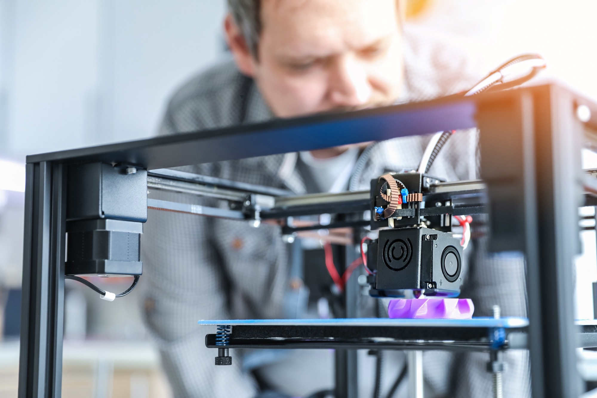 3D printer front field with a man out of focus behind it.