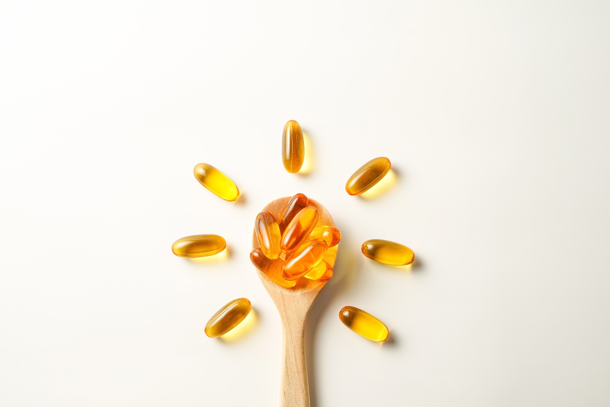Vitamin D capsules on a wooden spoon in the shape of the Sun.