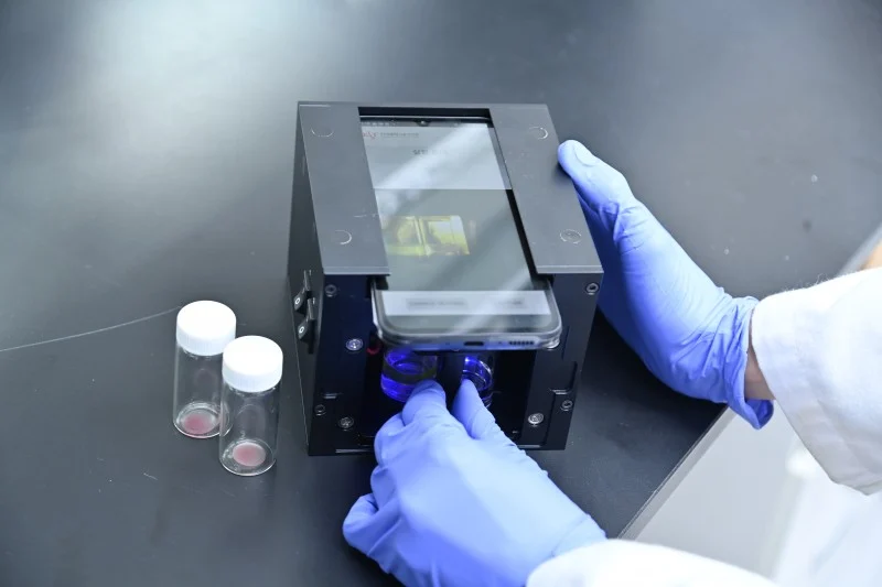 Photo of the kit. Includes a container with a film, a compact optical device for attaching a smartphone, and a diagnostic app.