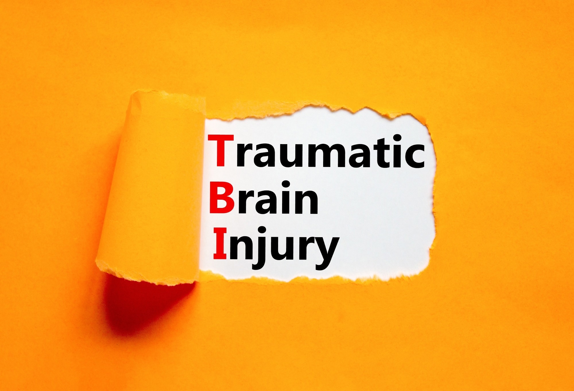 Concept words TBI traumatic brain injury on white paper on an orange background.