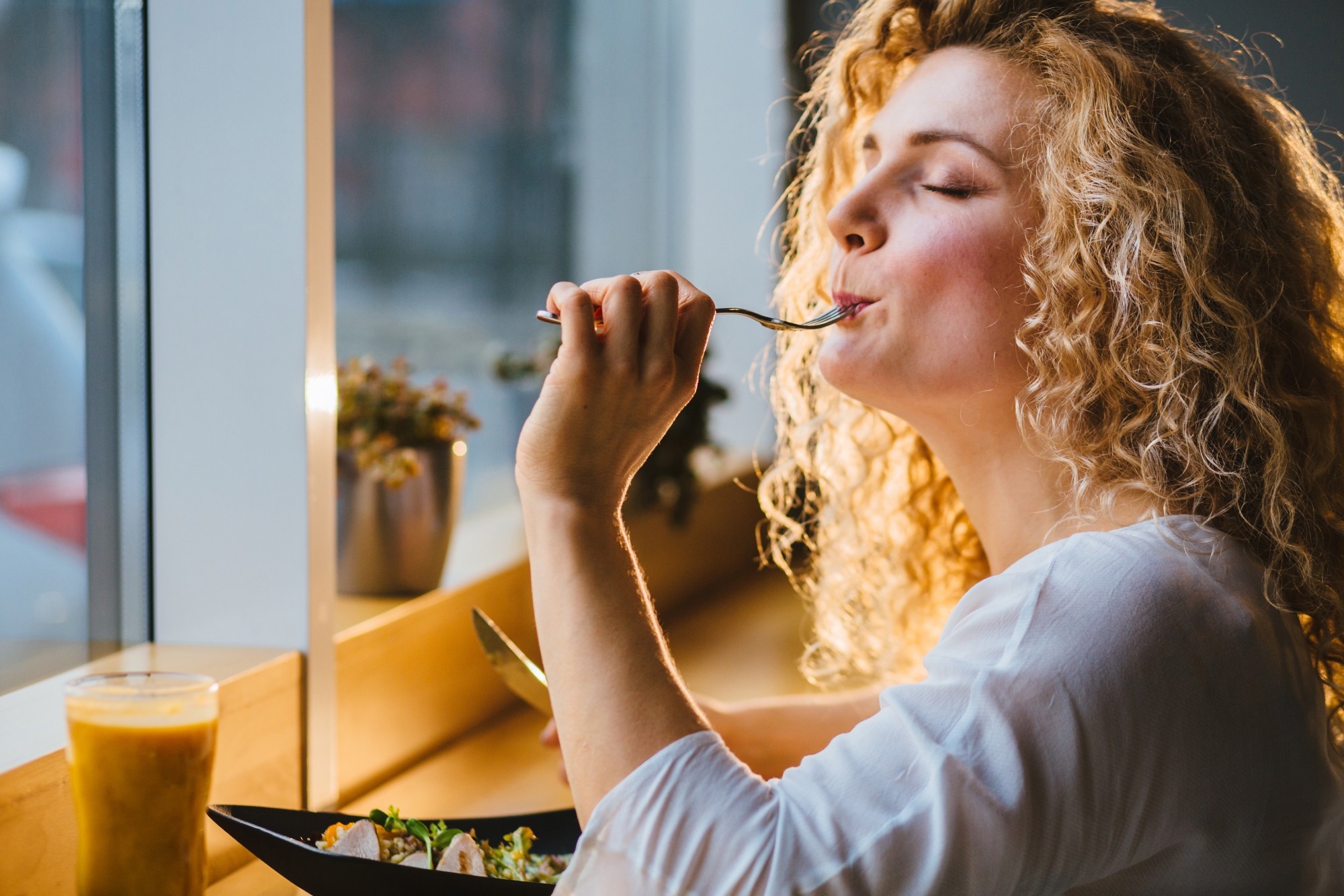 A woman tastes some food in a restaurant, closing her eyes in joy.
