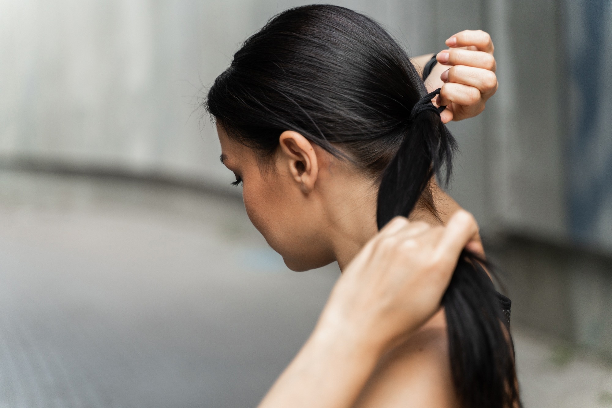 A woman with dark brown hair ties up her hair with a hairband.
