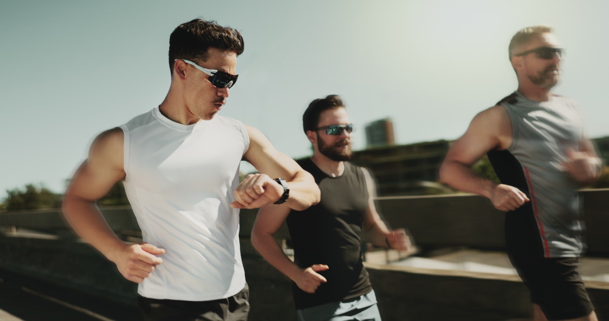 Three men running in an urban landscape. One checks his smart watch as he runs.