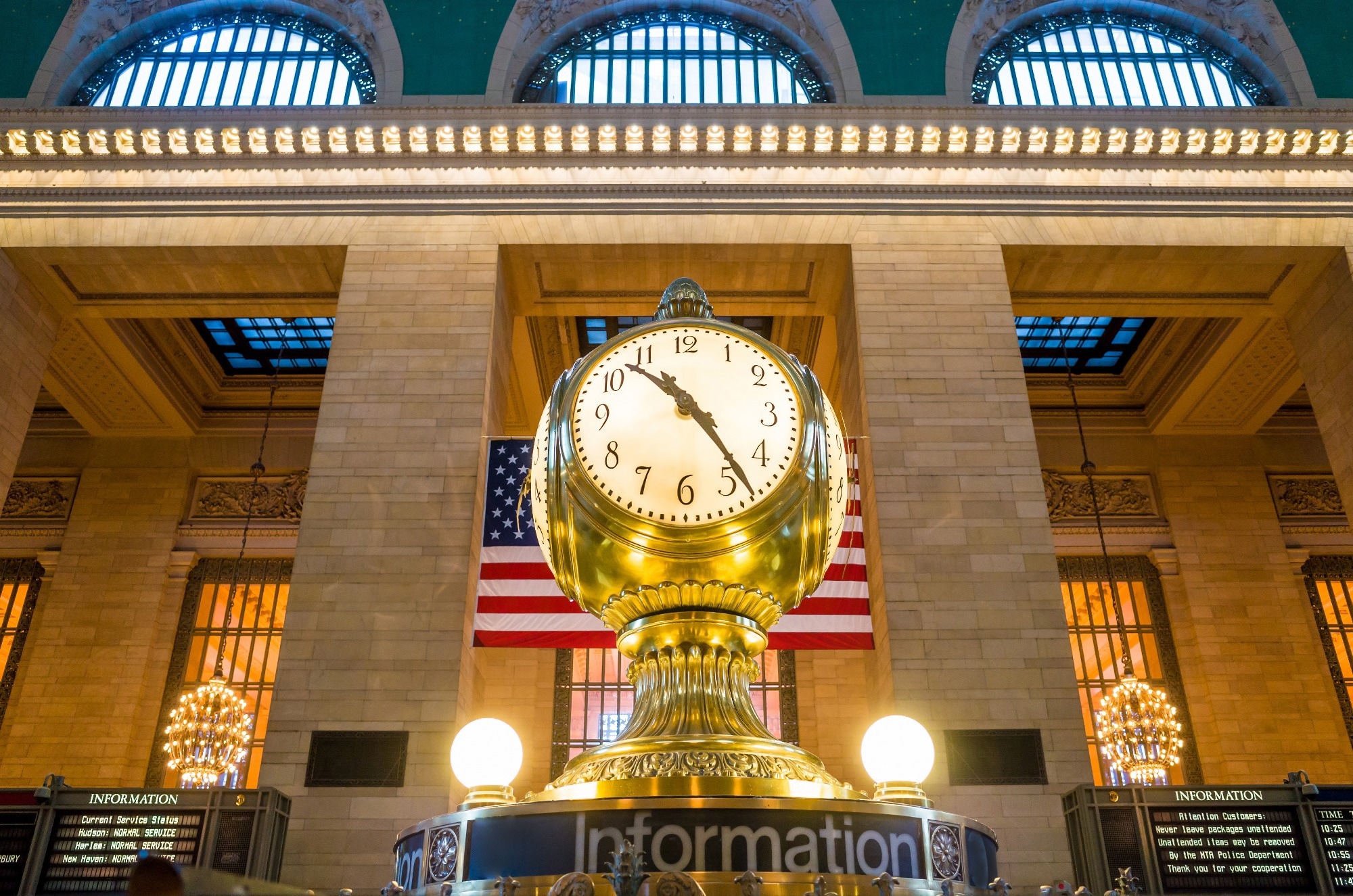 Grand Central station gold clock with train times on boards behind.