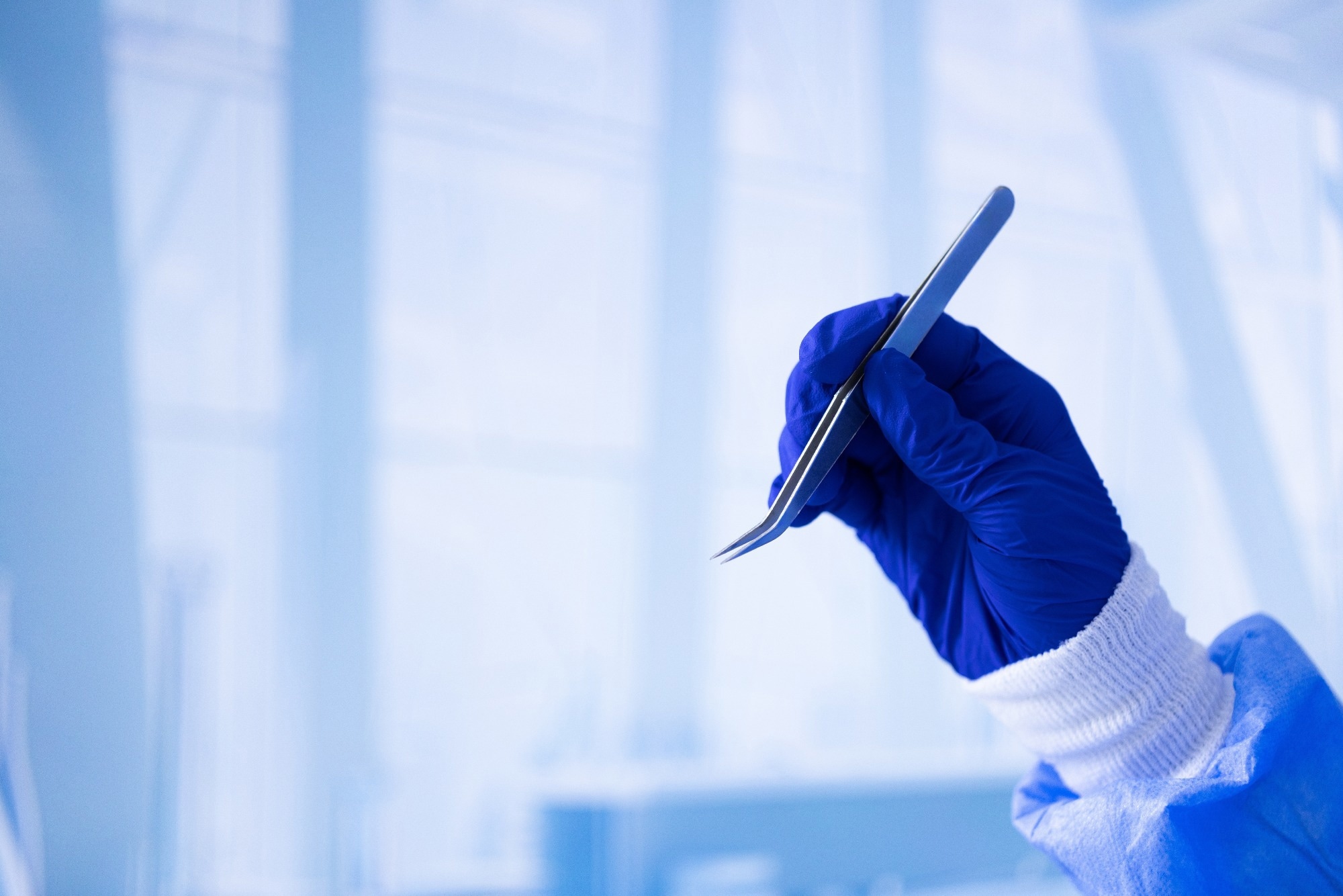 A person wearing a blue lab coat is holding a pair of tweezers. Concept of precision and attention to detail, as the person is likely using the tweezers for a scientific or medical purpose.