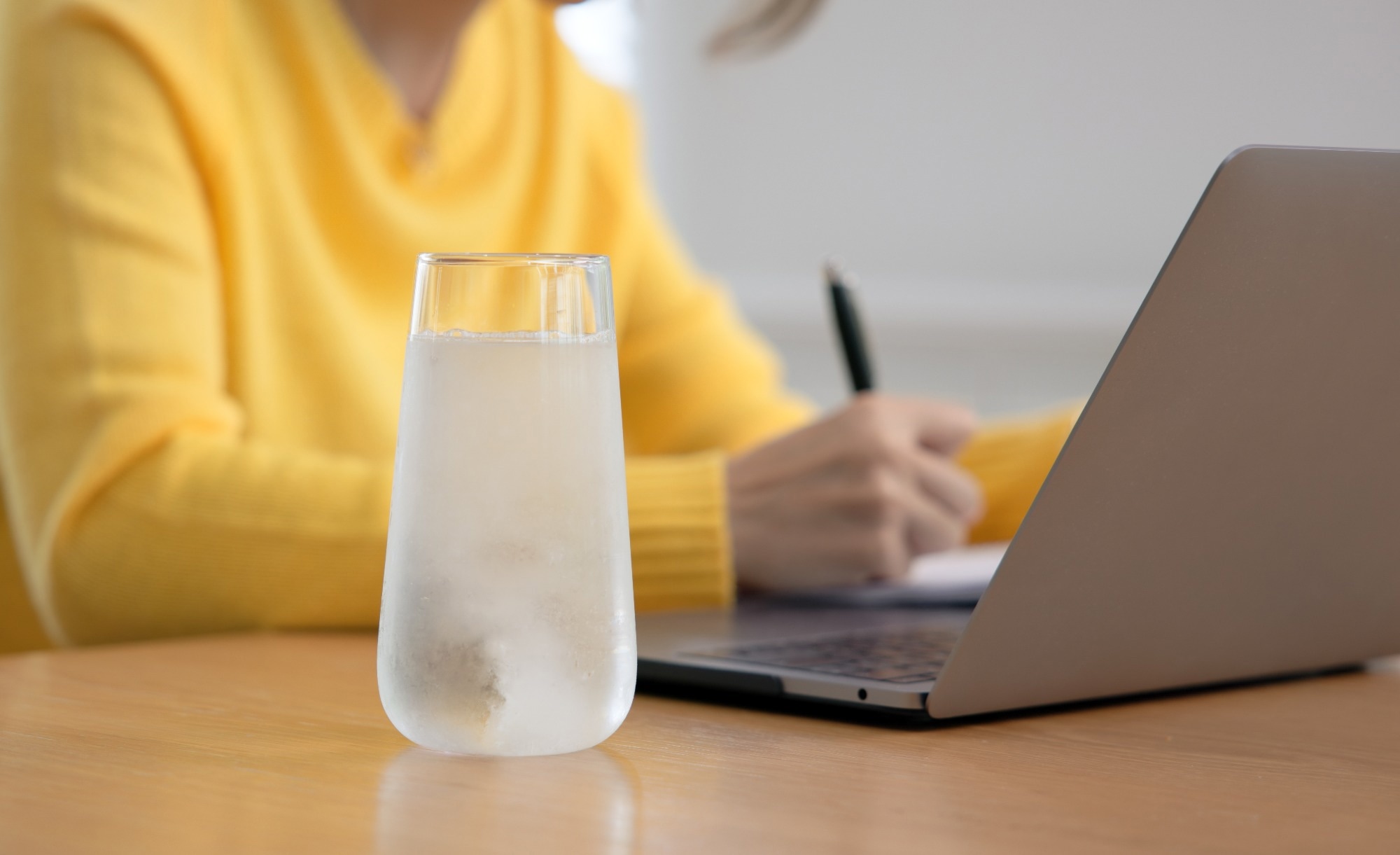 A cold glass of water next to a woman working on her laptop.