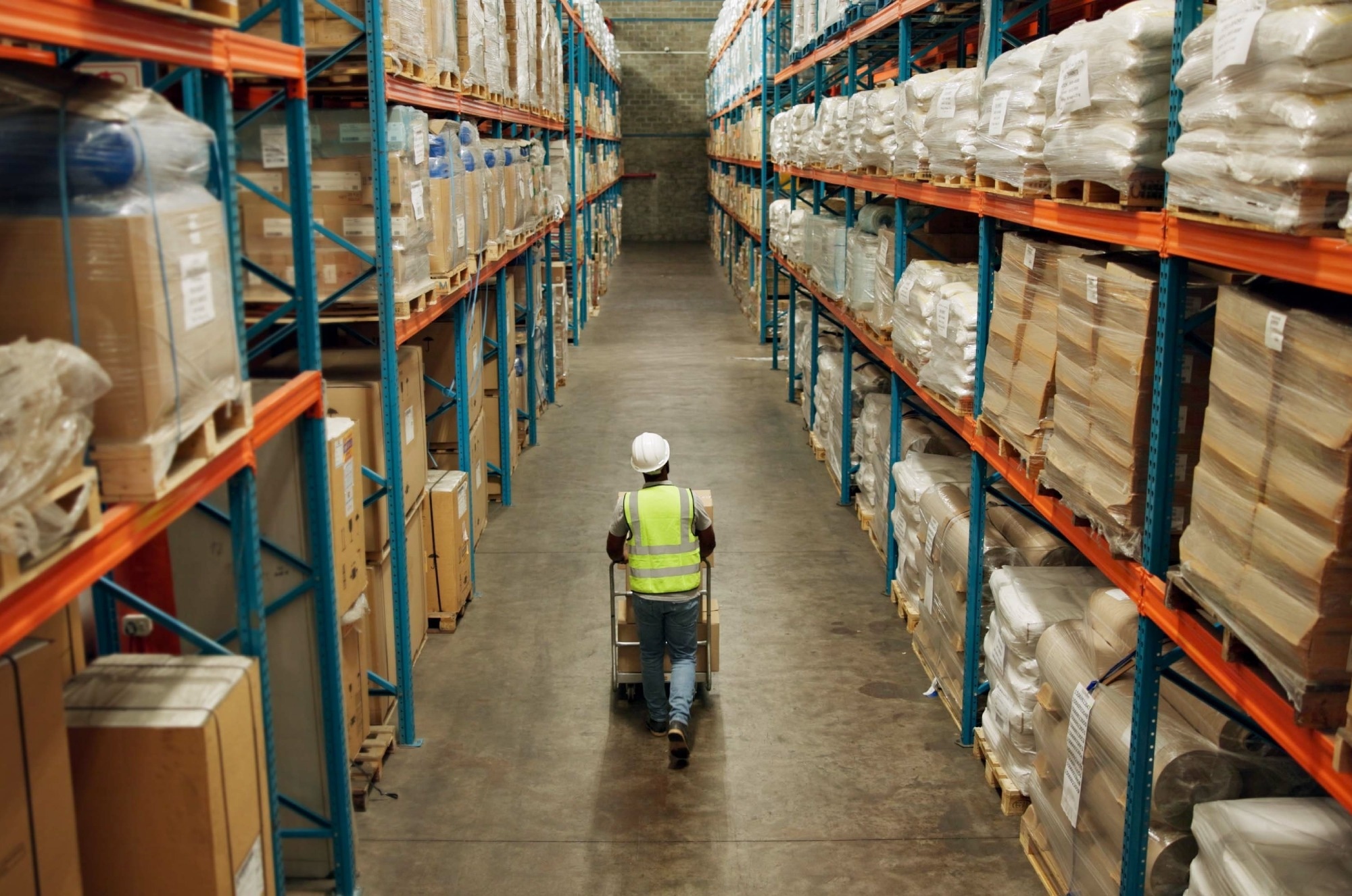 A worker in high vis and a hard hat walks down an aisle in a hardware store. The shot is taken from above, giving it a birds eye feel.