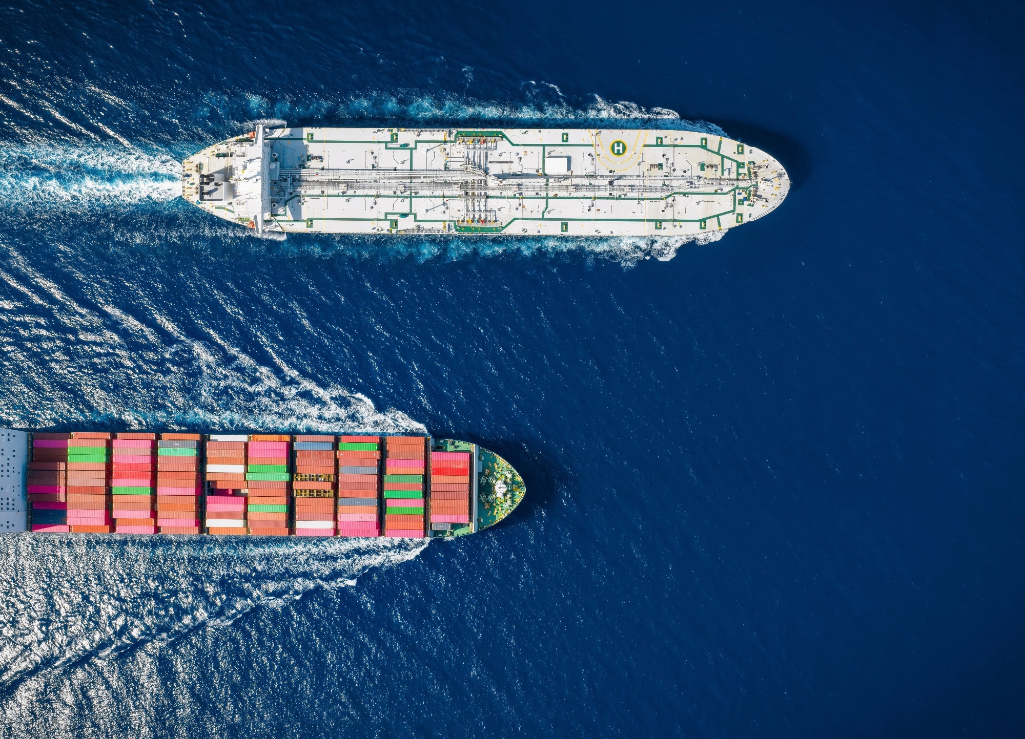 Aerial overhead view of a cargo container ship and a crude oil tanker crossing the ocean.