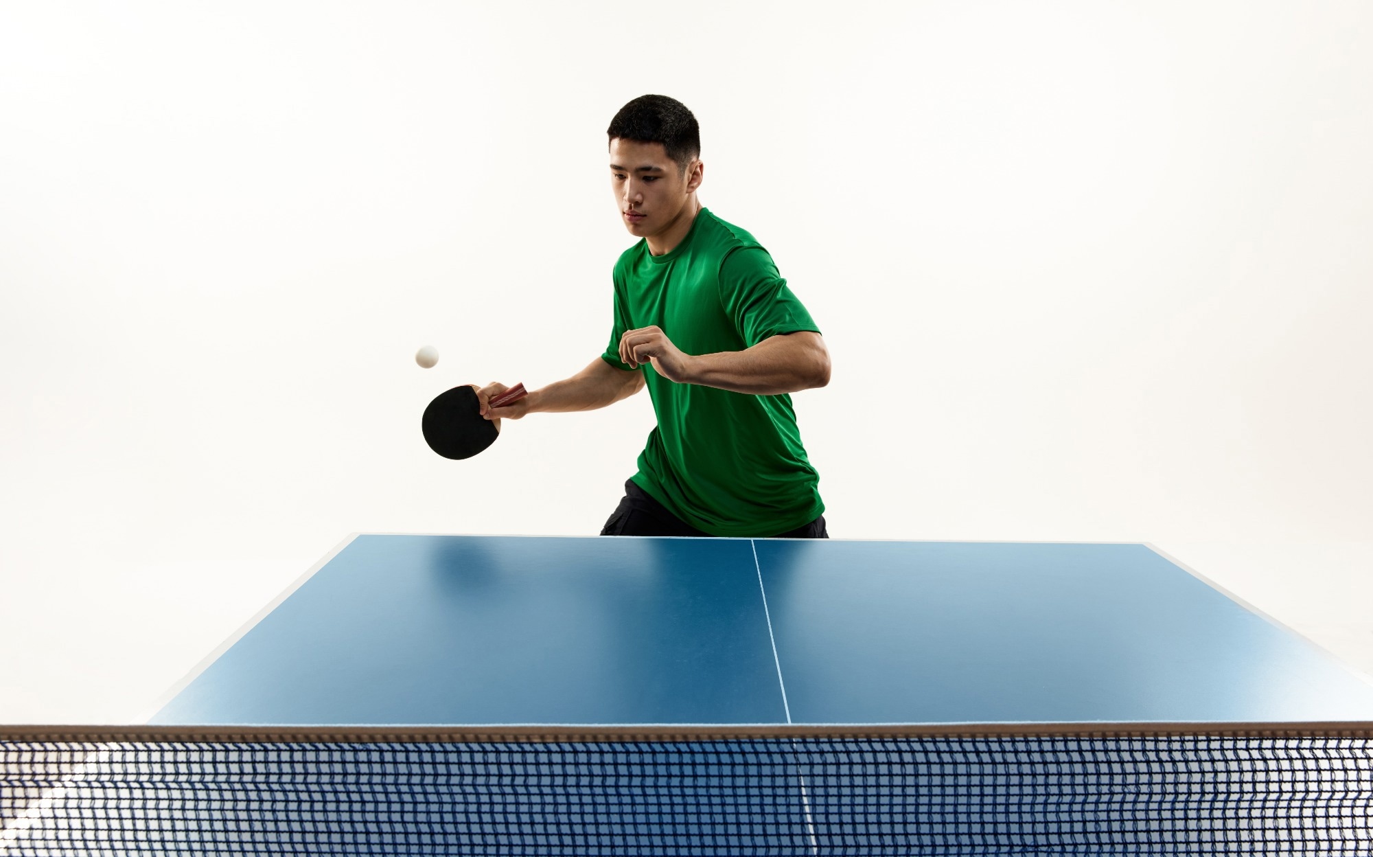 Focused table tennis serve from male table tennis player in vibrant green sportswear in motion against white studio background.