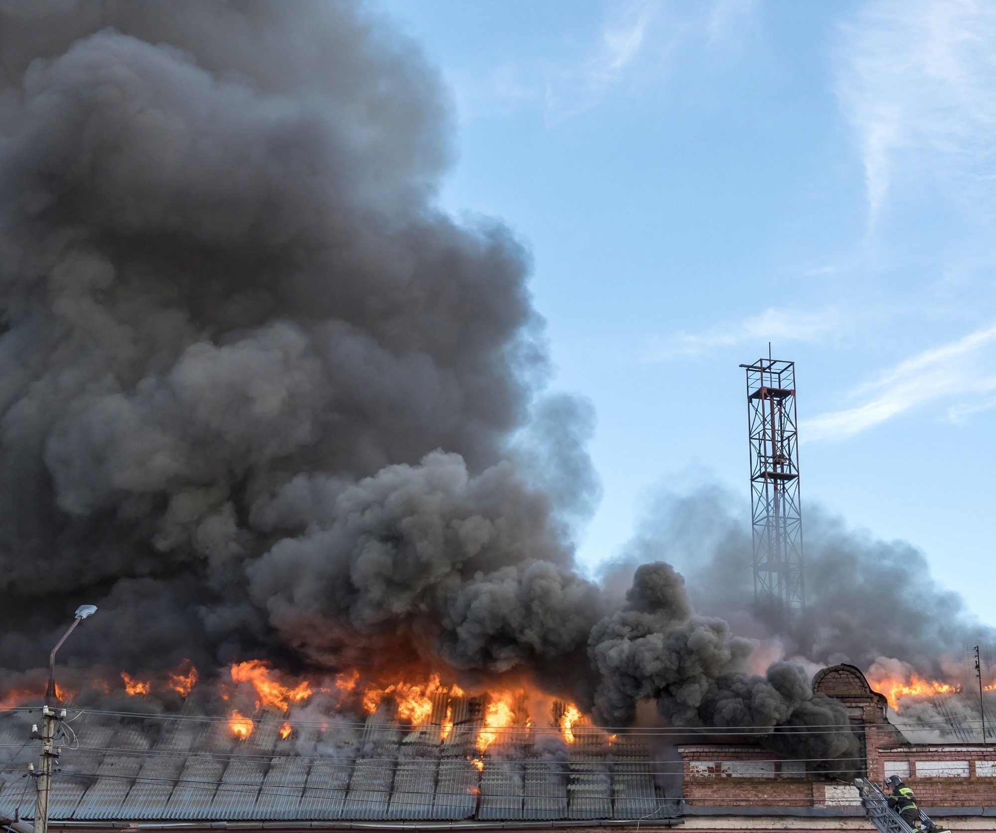Fire is burning in a building and the sky is blue. The fire is very large and is causing a lot of smoke