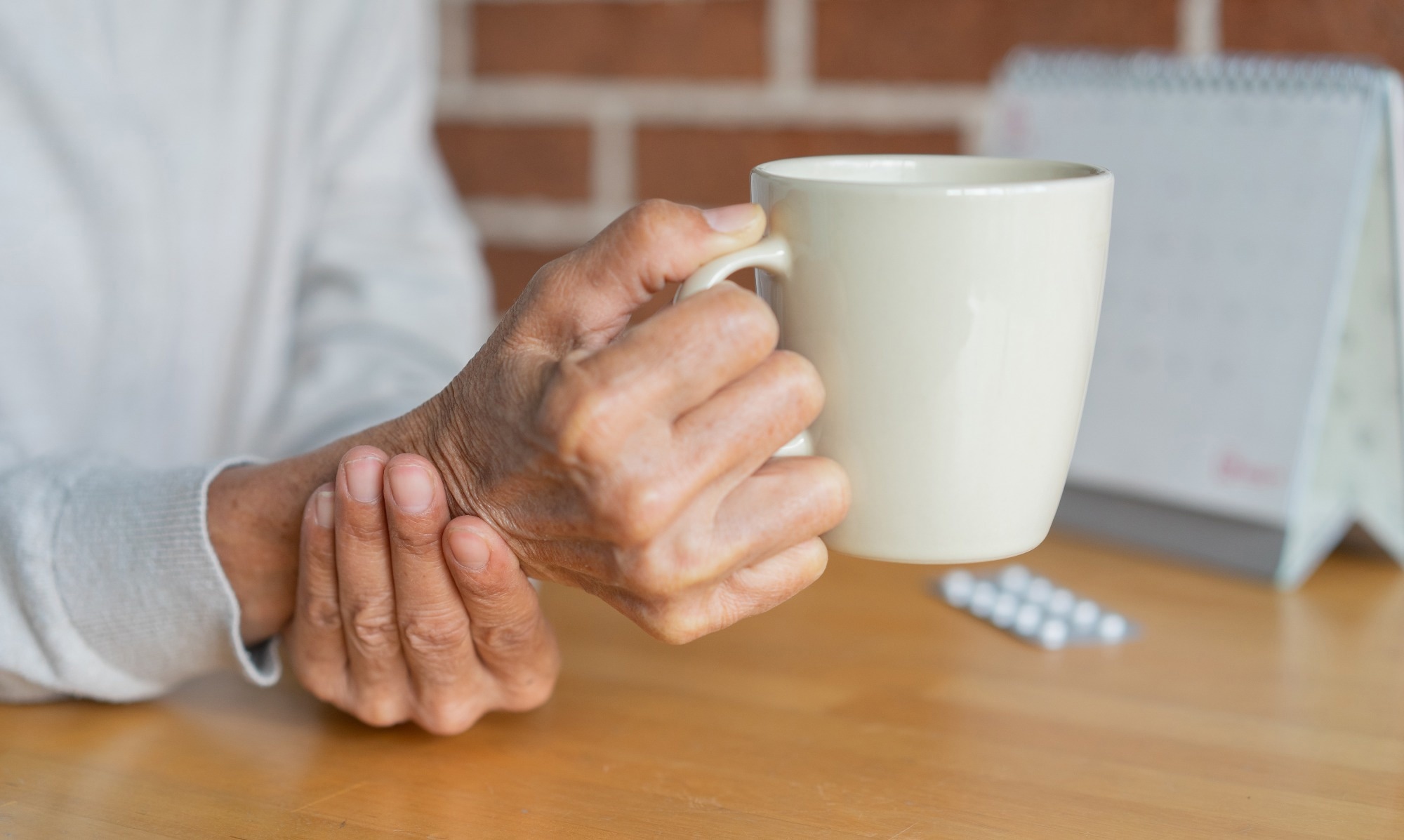 close up senior woman hold on hand to relief shaky symptom while drinking water
