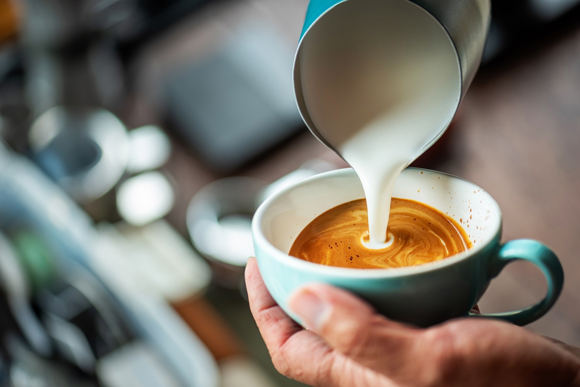 Barista pouring foamed milk into a cup of coffee