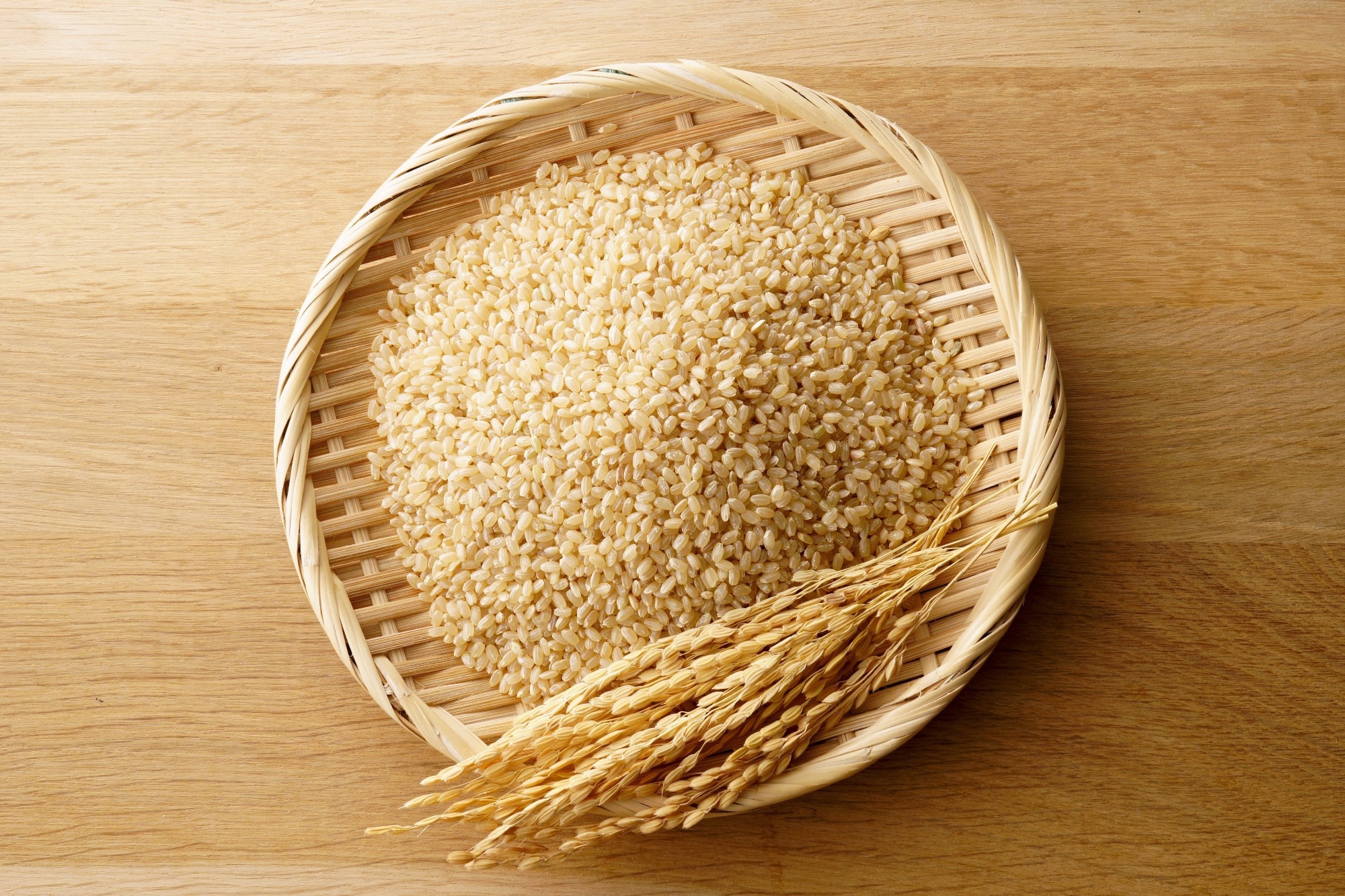 Brown rice grains on bamboo tray with rice ears on wooden background